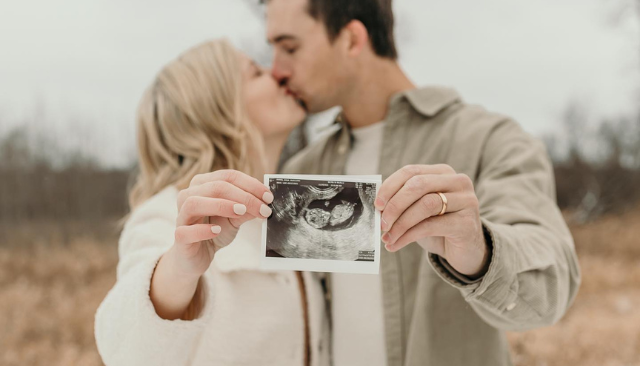 couple kissing and holding ultrasound picture in focus